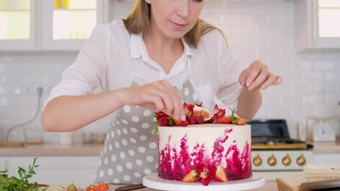 cooking and decoration of cake with cream. Young woman pastry chef in the kitchen decorating red velvet cake. Happy woman in apron in kitchen makes beautiful birthday cake, cooking and pastry skills