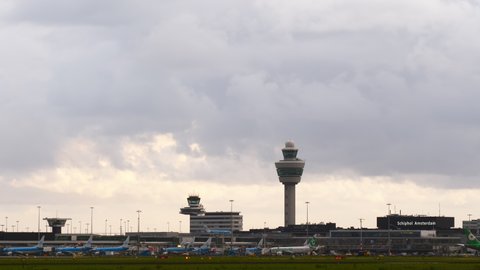AMSTERDAM - AUGUST 15, 2019: Overcast sky over Schiphol airport buildings, dark clouds slide fast, time lapse shot from distance. Many passenger airliners parked at apron, few planes taxiing at ramp