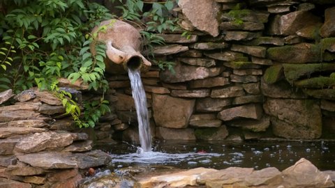 A small decorative mushroom fountain in a stone pool with a waterfall from a pitcher. Landscape design.	