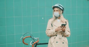Woman in protective mask, in helmet using her smartphone device, on green background. 4K video