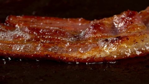 Close-up view of bacon slices in frying pan.