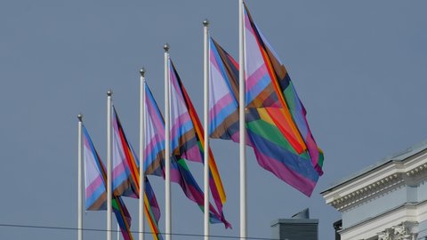 The Pride flags on a white flagpole against the blue sky.