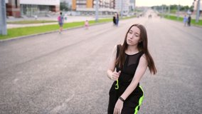 Video of an active young woman dancing hip hop choreography and break dance on a wide city street. Summer evening. Sunny sunset. Slow motion. Hand camera

