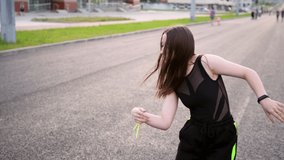 Video of an active young woman dancing hip hop choreography and break dance on a wide city street. Summer evening. Sunny sunset. Slow motion. Hand camera
