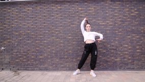Video of an active young woman dancing hip hop choreography and break dance outdoors against the wall. Slow motion. Gimbal shot
