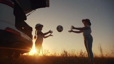 children in the park silhouette playing ball on vacation next to the car. happy family camping kid dreams concept. two sisters kid throw a ball each other play silhouette. girl kid on fun park
