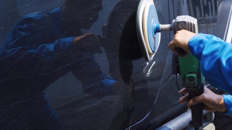 Close up of car mechanic using an orbital polisher and wax to polish a black car door. Shot in 4k resolution