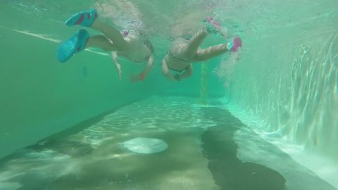 The camera is following two girls and boy swimming underwater in the pool