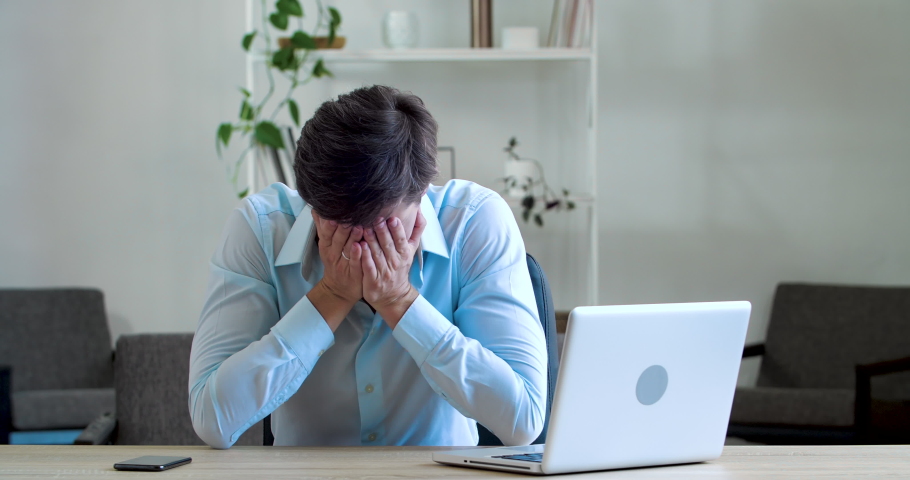 Frustrated young business man feels headache illness, soreness, thinks about difficult problem, worries about bad news or losing money, stress of hard work, fails sitting at table in office workplace | Shutterstock HD Video #1058787460