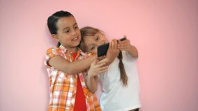 Two funny cute girls sisters learning using smartphone taking selfie at home, lenjoy social media app play game on a pink background, children and technology concept
