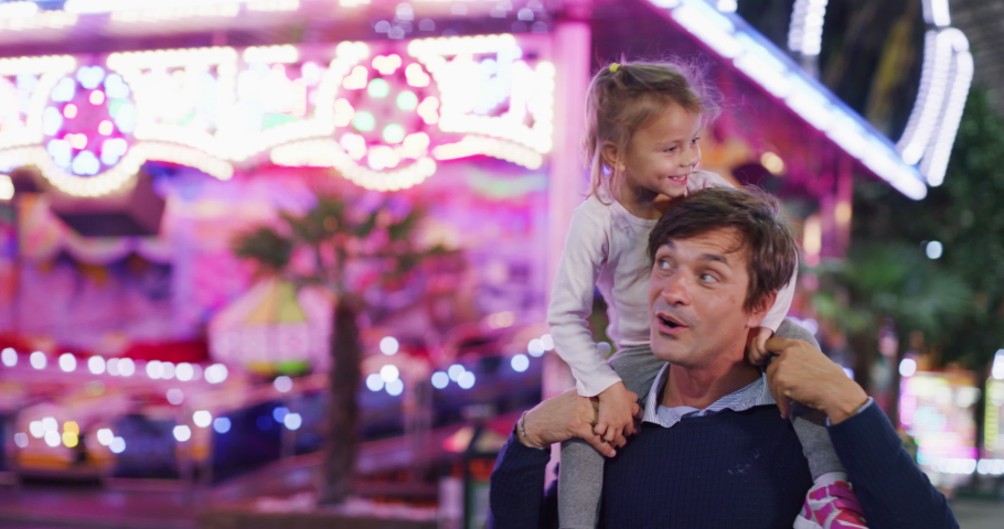Authentic shot of a happy smiling family is having fun together in amusement park with luna park lights at night. | Shutterstock HD Video #1058790043