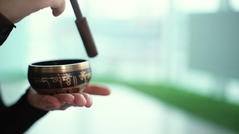 Close-up of woman hands playing on small Tibetan Singing Bowl with wooden stick. Concept of meditation zen practice with calm sounds. Shooting in slow motion.