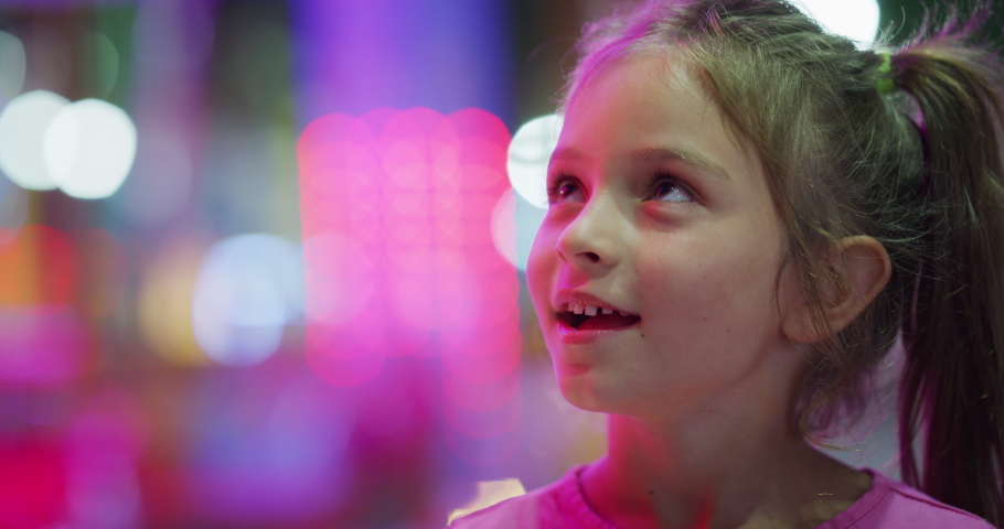 Authentic close up shot of a happy excited smiling little girl is having fun in amusement park with luna park lights at night. Royalty-Free Stock Footage #1058790334