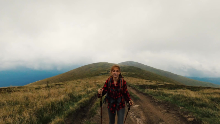 Young girl tourist on the trail in mountains with trekking sticks