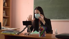 A young teacher leads a lesson, filming himself on a smartphone. Masked teacher. Video tutorial during quarantine.Covid-19.Finger counting.