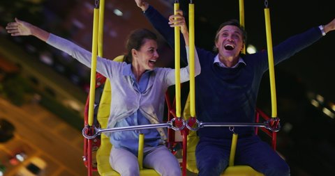 Authentic close up shot happy carefree exited smiling couple in love is having fun and enjoy chain swing carousel riding together in amusement park at night.