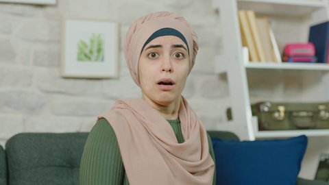 Young muslim woman is afraid of something while sitting at home. Portrait of a scared muslim woman. Young muslim woman with skin problem.Close up.Slow motion video.