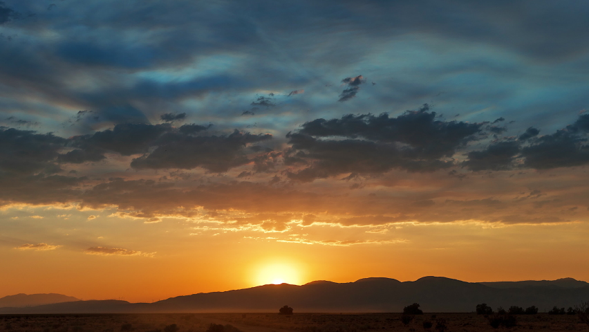 The suns sets in majestic splendor over the Mojave Desert landscape and rugged mountain range in the time lapse Royalty-Free Stock Footage #1058800375