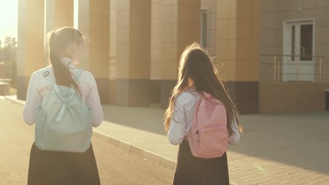 girlfriends go to school. They have lot of fun. School Girls with backpacks go to school on street. education concept. healthy teenagers go to class outdoors. girls chat and talk in the schoolyard