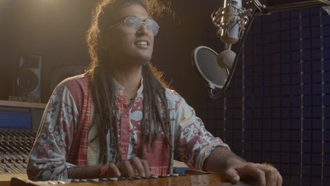 Music production studio. Creative world. Hindi man playing harmonium in the sound studio. A long hair brunette male person in a traditional shirt plays meditation music.