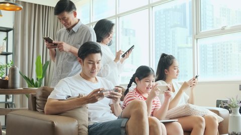 Happy young asian big family relaxing on couch with adorable small daughter and grand father grand mother hand using smartphone application together in living room,family smartphone addiction
