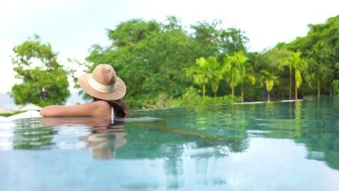 A woman wearing a hat, relaxing in an infinity pool at a luxury hotel.