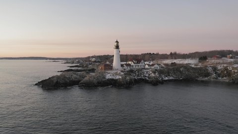 Lighthouse flashing above rocky coastal outcrop, winter sunrise, STATIONARY AERIAL.