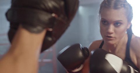 Cinematic shoot of boxing in the ring, woman fighter trains punches and punching focus mitts, training day with trainer in the boxing gym, 4k slow motion.