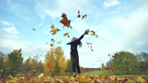 A young girl schoolgirl whirls with autumn leaves in the city park.