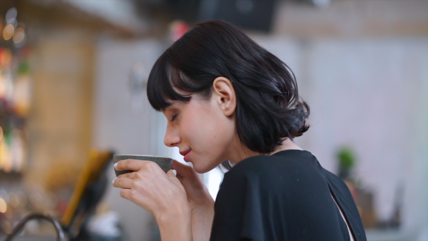 Close up and slow motion shot of short dark hair European woman with white skin sits and enjoys smelling a dark grey cup of coffee and feeling appreciate at coffee bar in cafe restaurant. | Shutterstock HD Video #1058810428