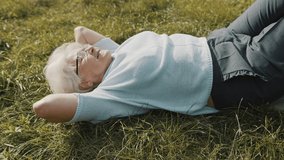 Cool grandma lying on the grass with hands under her head. Resting in nature. High quality 4k footage