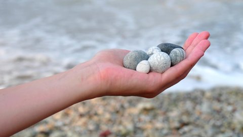 Beautiful round gray and white sea stones lie in a female hand against the background of the sea and waves. The concept of relaxation, vacation and meditation, zen. Island of Cyprus.