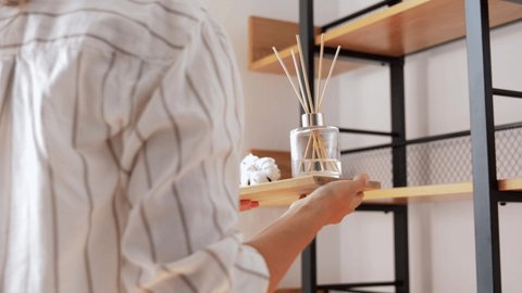 home improvement, decoration and people concept - woman placing aroma reed diffuser to shelf