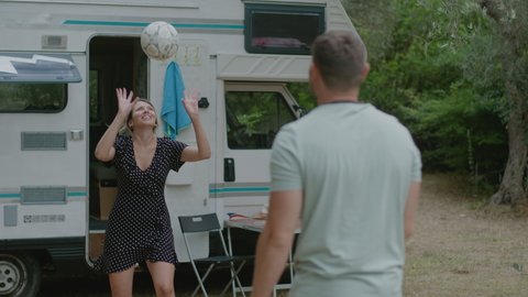 Pretty couple play volleyball together in nature enjoyng vacation near motor home RV campervan. Traveling in recreational vehicle.
