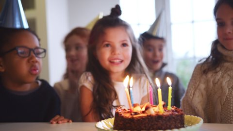 Girl Celebrating Birthday With Friends At Home Blowing Out Candles On Party Cake