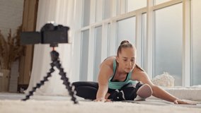 Young Girl Shooting Her Fitness Videoblog. Young Girl Conduct Remote Teaching to Training Online During Blogging. Girl Shooting a Video Blog While Doing Exercises of Stretching on Mat in Bright Room.