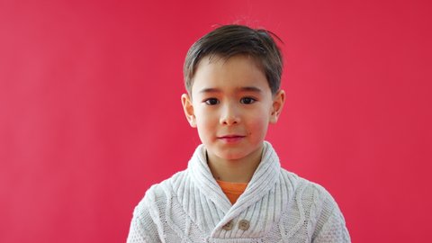 Portrait Of Young Boy Against Red Studio Background Pulling Funny Faces At Camera