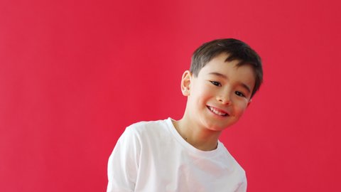 Young Boy Jumps Up Into Frame Against Red Studio Background Smiling And Laughing At Camera