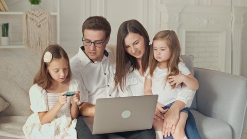 Happy Family Uses a Laptop For Online Shopping, Sitting on the Couch at Home. Parents With Children Use a Credit Card for Online Shopping. Binding a Card for Online Shopping