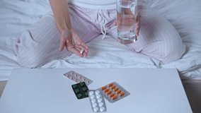 cropped view of woman holding pill and glass of water near blister packs
