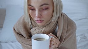 sick young woman holding cup of hot tea and looking at camera