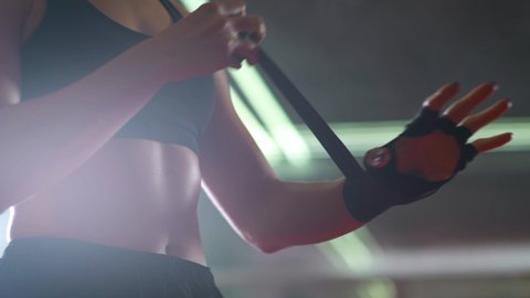 Woman fighter wraps her hands with boxing bandages, kickboxing training day in a gym, neon lighting.