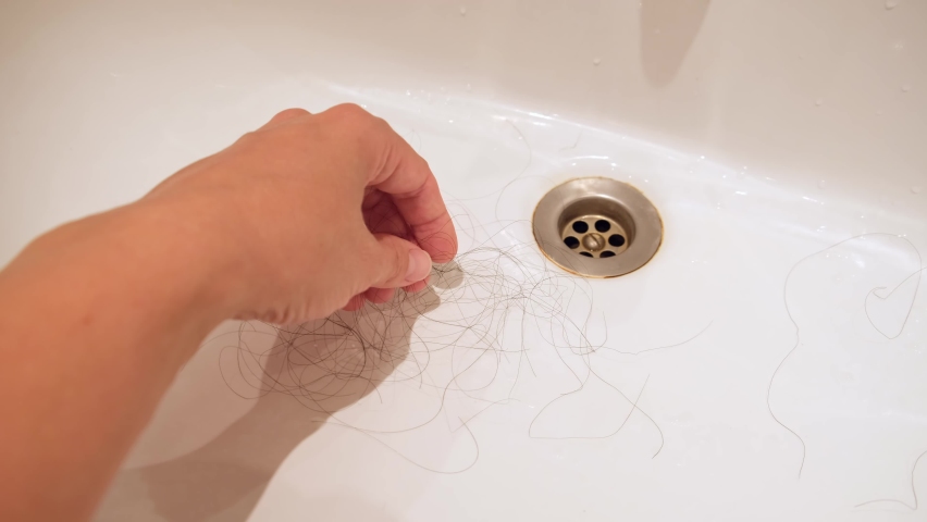 A hand collecting dark long female fallen hair in a washing bowl, hair loss after washing and brushing hair, androgenic alopecia.