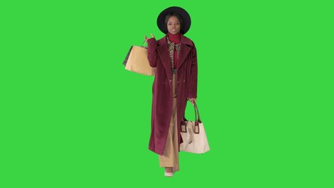 Pretty African american fashion girl in coat and black hat strolling with shopping bags on a Green Screen, Chroma Key.