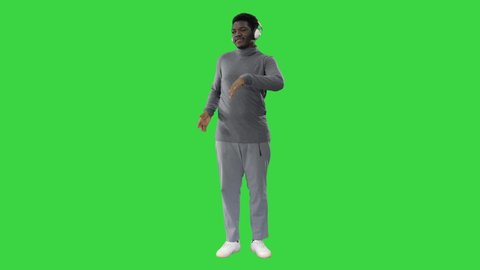 Passionate African american man listening to the music in headphones and dancing on a Green Screen, Chroma Key.