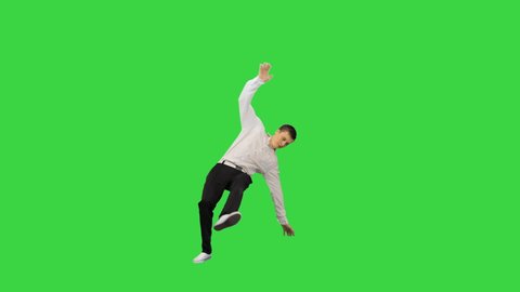 Young man dressed in white shirt and black pants jumping in the frame and starting to dance break looking at camera on a Green Screen, Chroma Key.