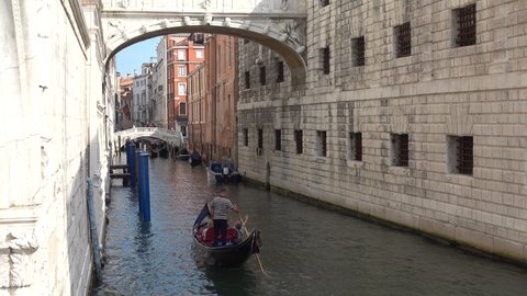 Venice, bridge of sighs, gondola floats out from under it. The gondolier and passengers are on their backs, their faces are not visible. The gondolier points to the Bridge of Sighs, explains something