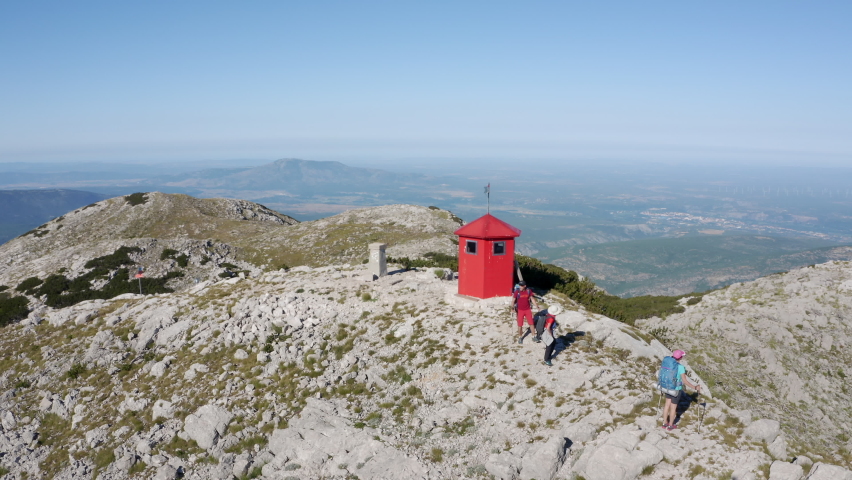 4K three travellers with backpacks on top of Dinara mountain near red booth. Travel concept, backpacking, mountaineering concept.