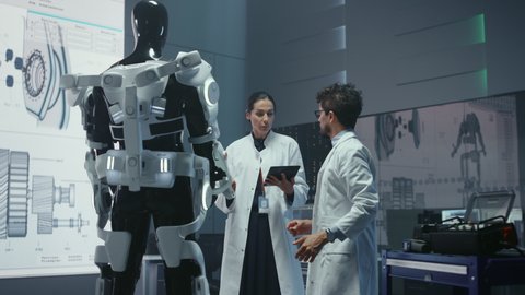In Robotics Development Laboratory: Chief Female Engineer and Top Male Scientist Work on a Bionics Exoskeleton Prototype. Designing Powered Exosuit to Help Disabled People, Hard Labor Workers	