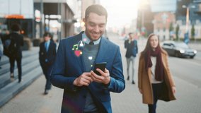 Young man Uses Smartphone with Animated Social Media Icons Flying Away, Walks on Crowded City Streets. Social Network Concept, Likes, Emoticons, e-business. Front View Following Shot - Powered by Shutterstock - Get 15% off with code: PIKWIZARD15